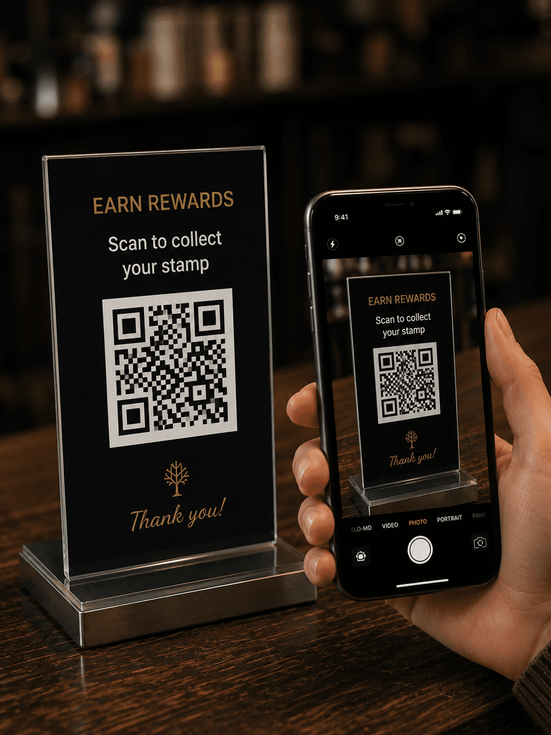 Customer holding their phone next to the Qafey 'Earn Rewards' QR stand on a café counter, framing it inside the camera viewfinder.